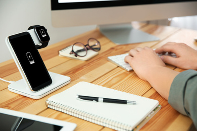 Photo of Man working at table while his mobile phone and smartwatch charging with wireless device