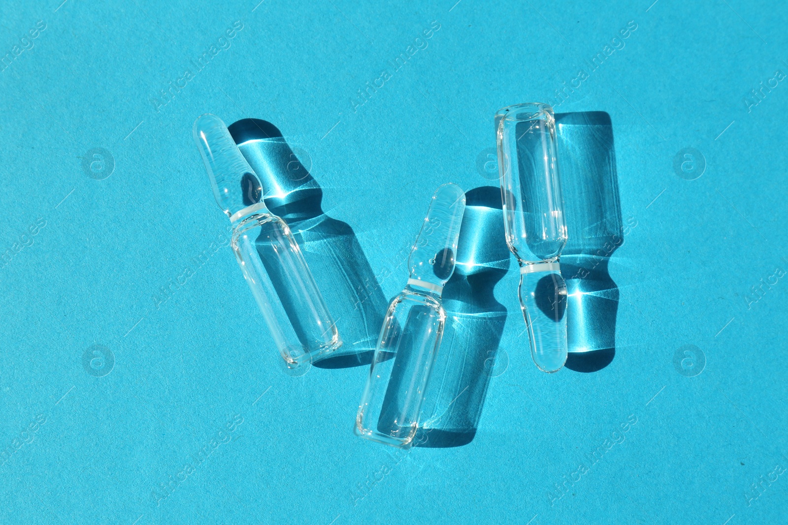 Photo of Glass ampoules with liquid on light blue background, top view