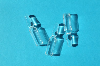 Glass ampoules with liquid on light blue background, top view