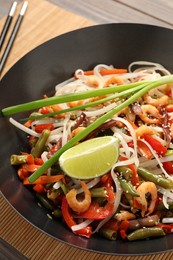 Photo of Shrimp stir fry with noodles and vegetables in wok on table, closeup