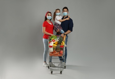 Photo of Family in medical masks with shopping cart full of groceries on light grey background