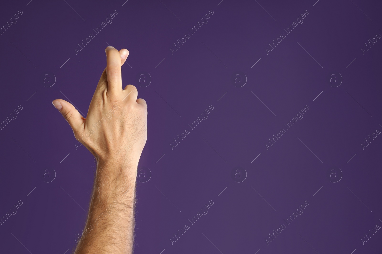 Photo of Man with crossed fingers and space for text on purple background, closeup. Superstition concept