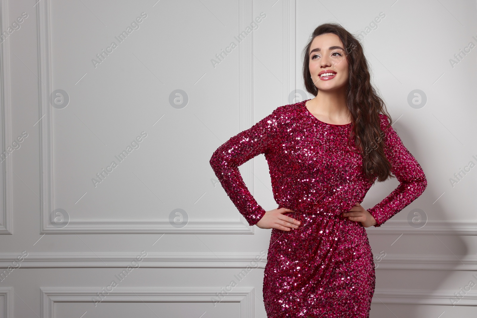 Photo of Beautiful young woman in stylish pink sequin dress near white wall indoors, space for text. Party outfit