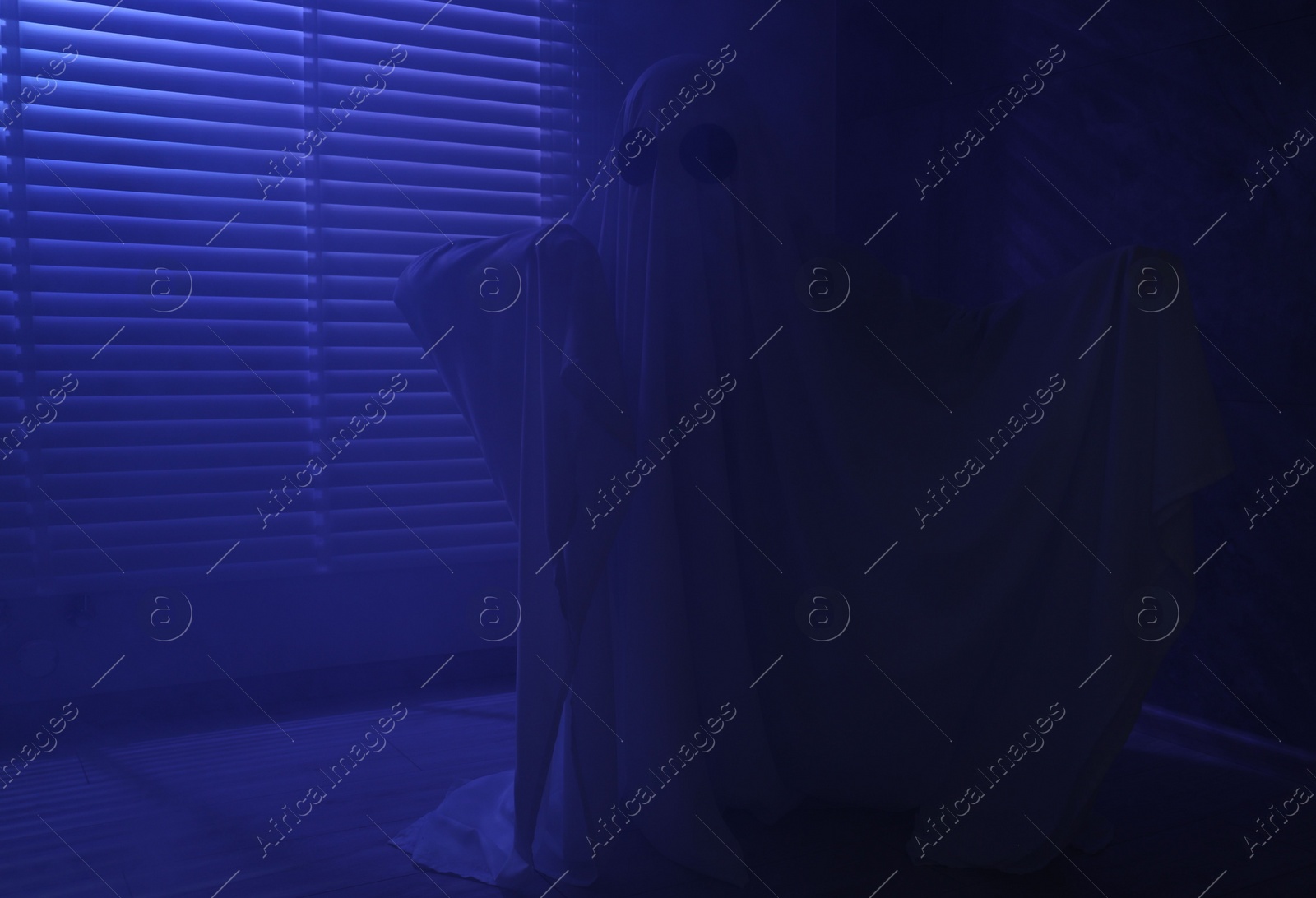 Photo of Creepy ghost. Woman covered with sheet near window in blue light