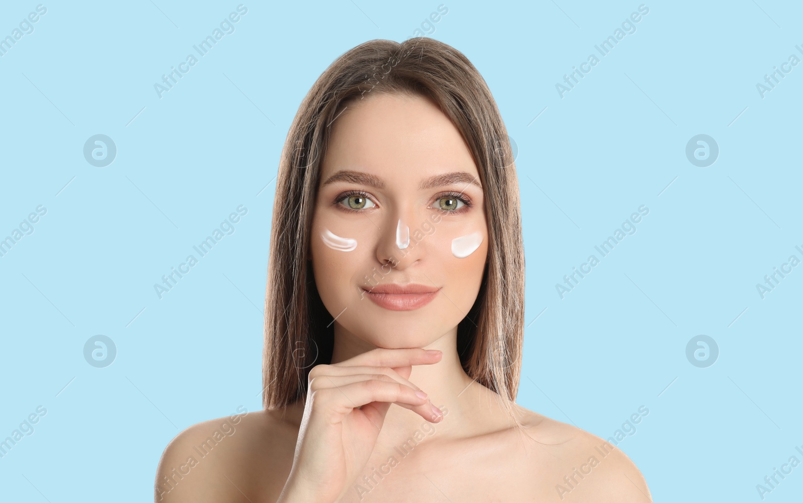 Image of Young woman with sun protection cream on face against light blue background