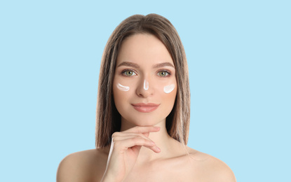 Image of Young woman with sun protection cream on face against light blue background