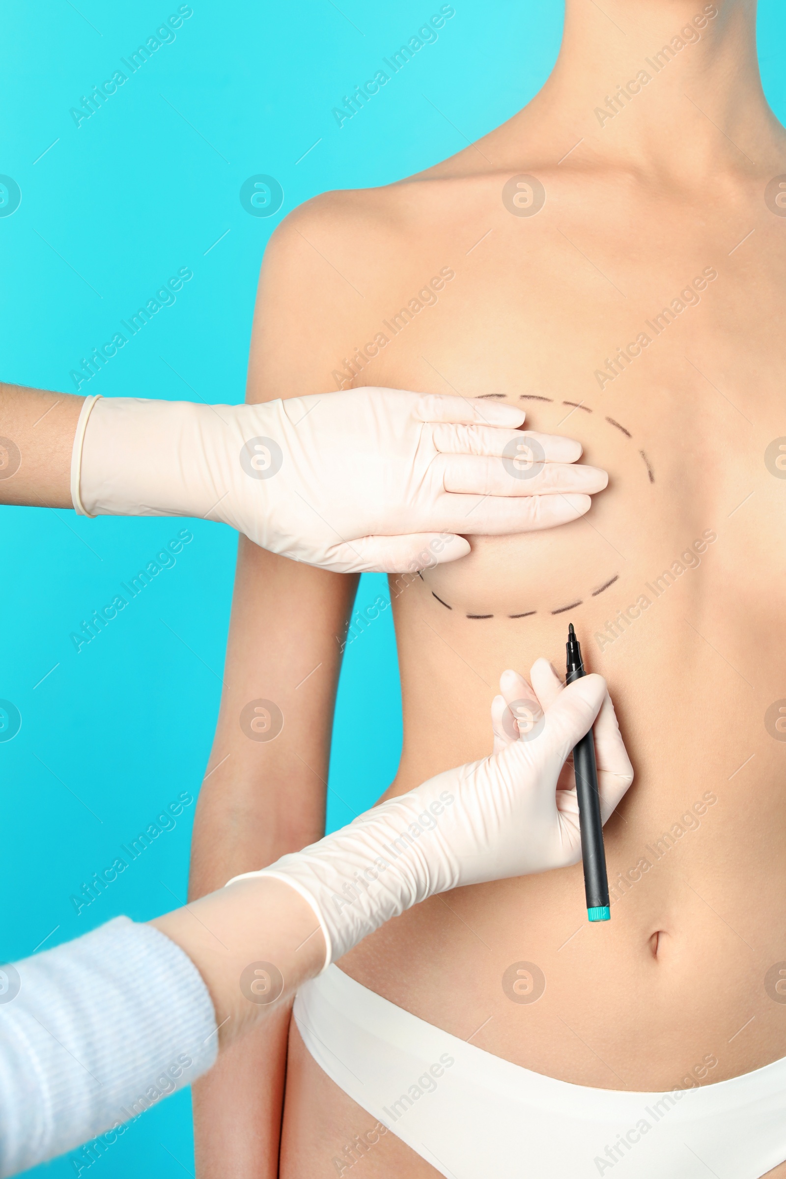 Photo of Doctor drawing marks on patient's breast for cosmetic surgery operation against color background, closeup