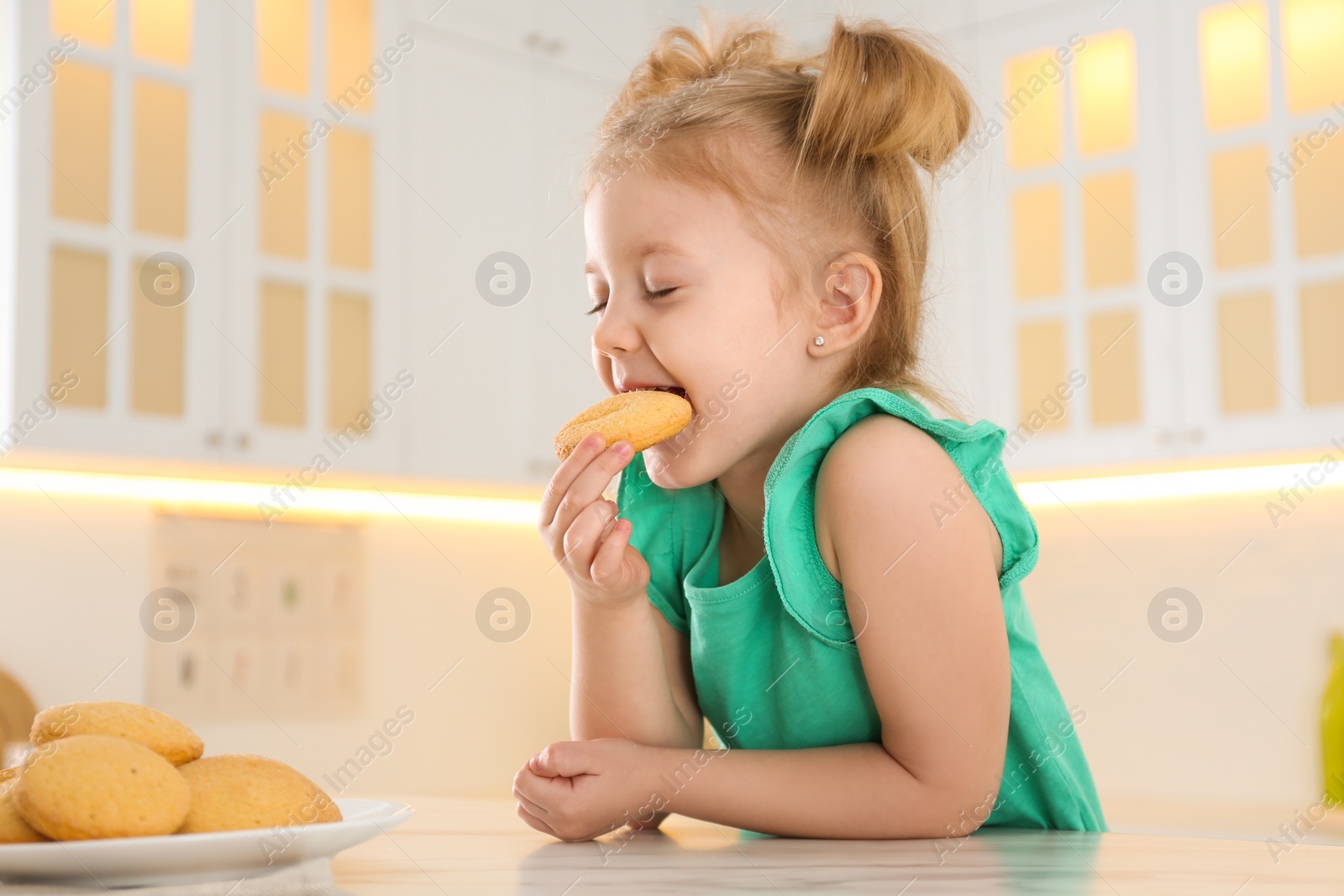 Photo of Cute little girl eating cookies in kitchen