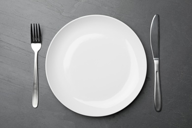 Photo of Stylish ceramic plate and cutlery on dark background, flat lay