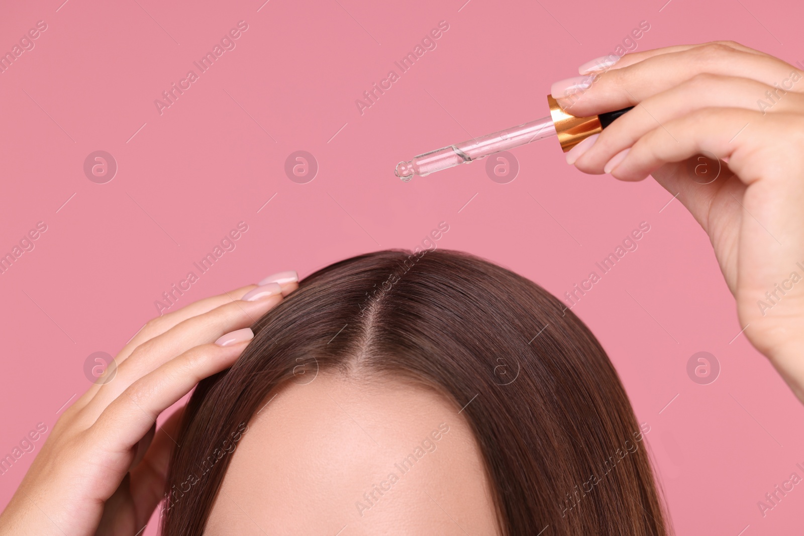 Photo of Woman applying serum onto hair on pink background, closeup