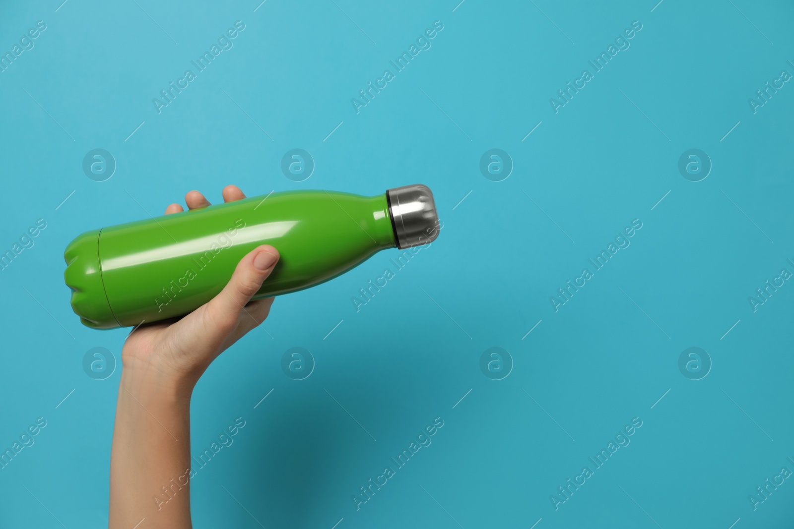 Photo of Woman holding modern green thermos on light blue background, closeup. Space for text