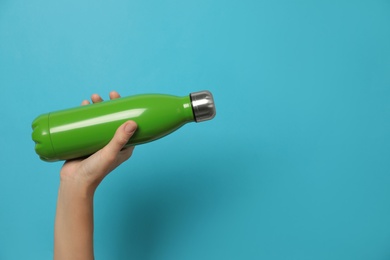 Photo of Woman holding modern green thermos on light blue background, closeup. Space for text