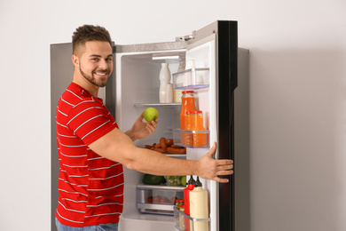 Photo of Young man taking fresh apple out of refrigerator