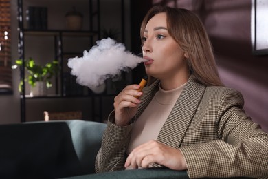 Photo of Beautiful young woman using disposable electronic cigarette indoors