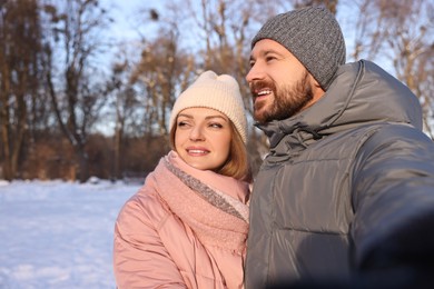 Photo of Happy couple taking selfie in sunny snowy park. Space for text