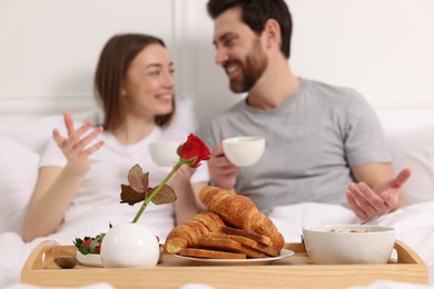 Photo of Tray with tasty breakfast in bed. Happy couple drinking coffee, selective focus