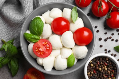 Delicious mozzarella balls, tomatoes and basil leaves on light gray table, flat lay.