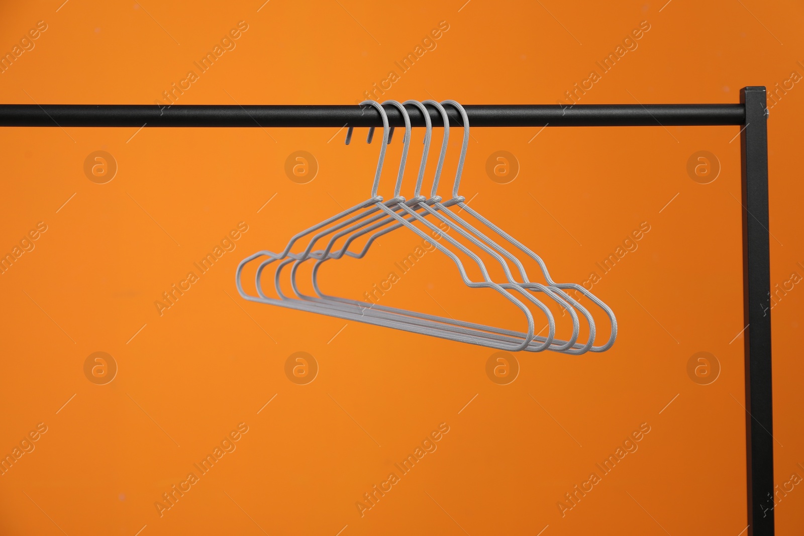 Photo of Empty clothes hangers on rack against orange background