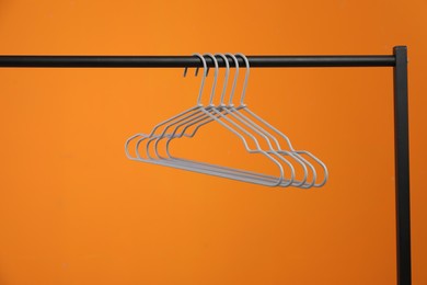 Photo of Empty clothes hangers on rack against orange background