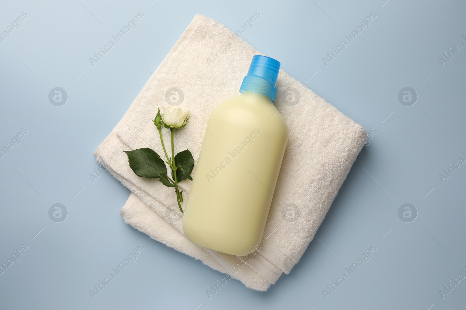 Bottle of fabric softener, terry towel and beautiful rose on light background, top view Photo of Bottle of fabric softener, terry towel and beautiful rose on light background, top view