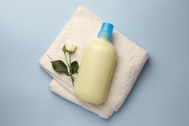 Photo of Bottle of fabric softener, terry towel and beautiful rose on light background, top view