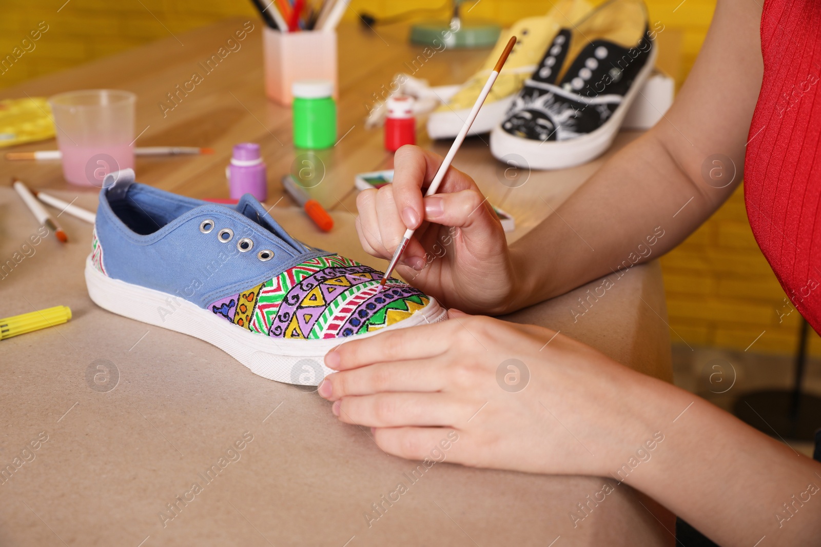 Photo of Woman painting on sneaker at wooden table indoors, closeup. Customized shoes