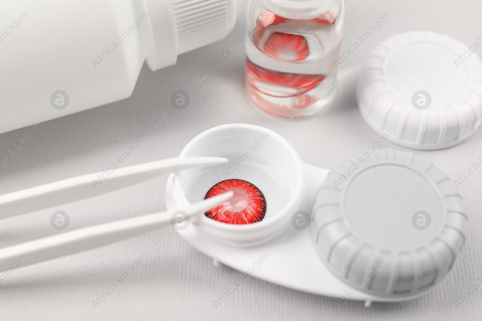 Photo of Case with red contact lenses, bottle of solution and tweezers on light grey background