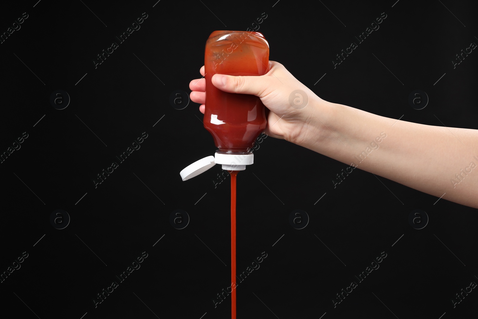 Photo of Woman pouring tasty ketchup from bottle on black background, closeup