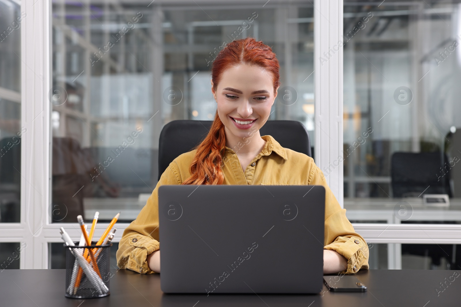 Photo of Happy woman working with laptop at black desk in office