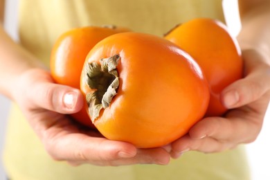 Woman holding delicious ripe juicy persimmons on light background, closeup