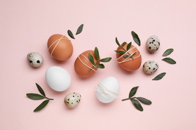 Photo of Beautifully decorated Easter eggs and green leaves on pale pink background, flat lay