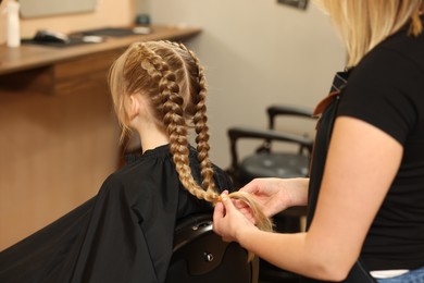 Professional hairdresser braiding girl's hair in beauty salon