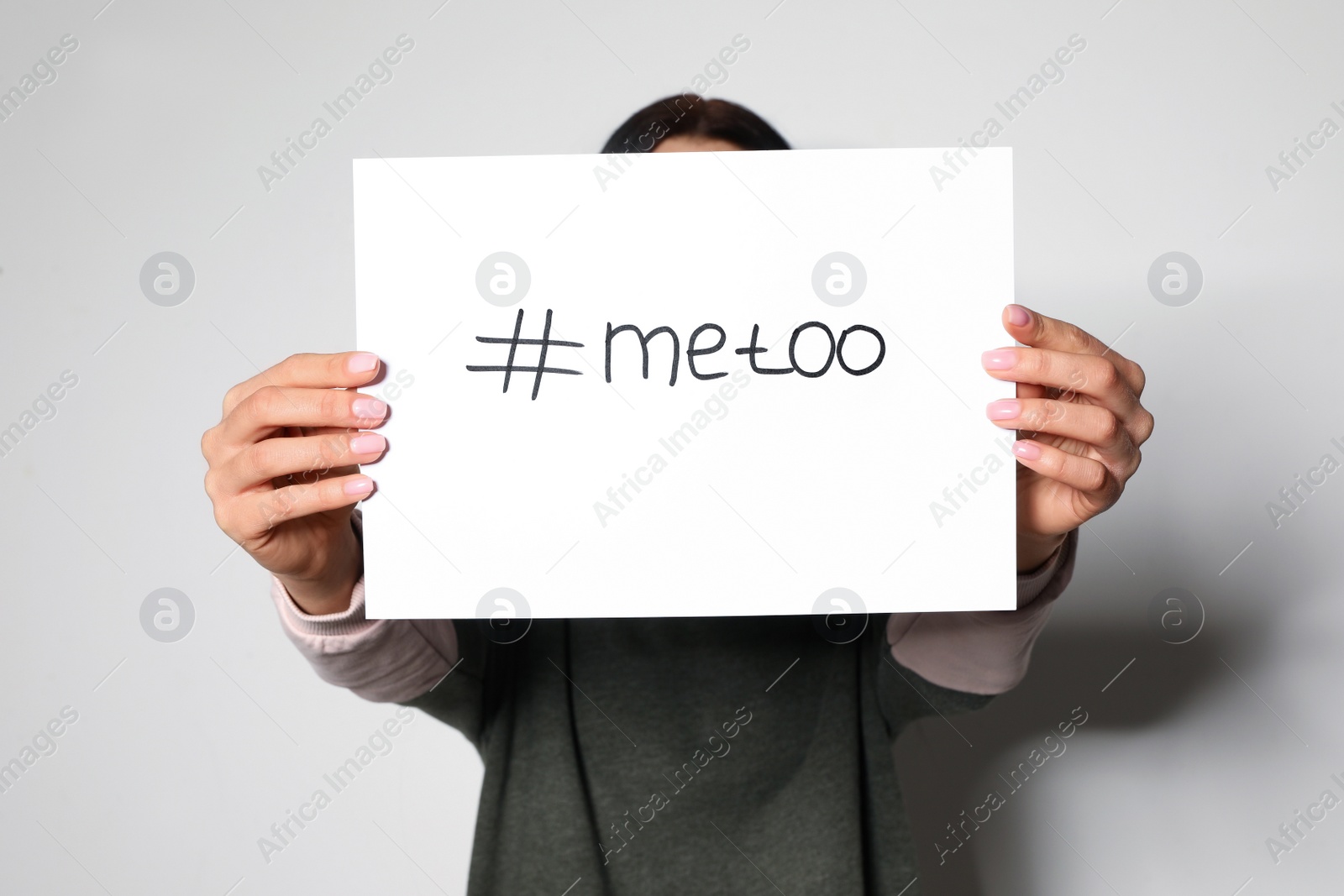 Photo of Young woman holding #METOO card against light background