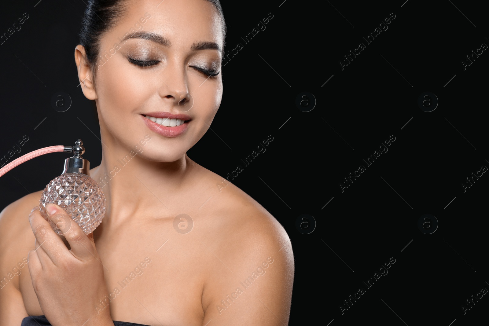 Photo of Young woman with bottle of perfume on black background. Space for text