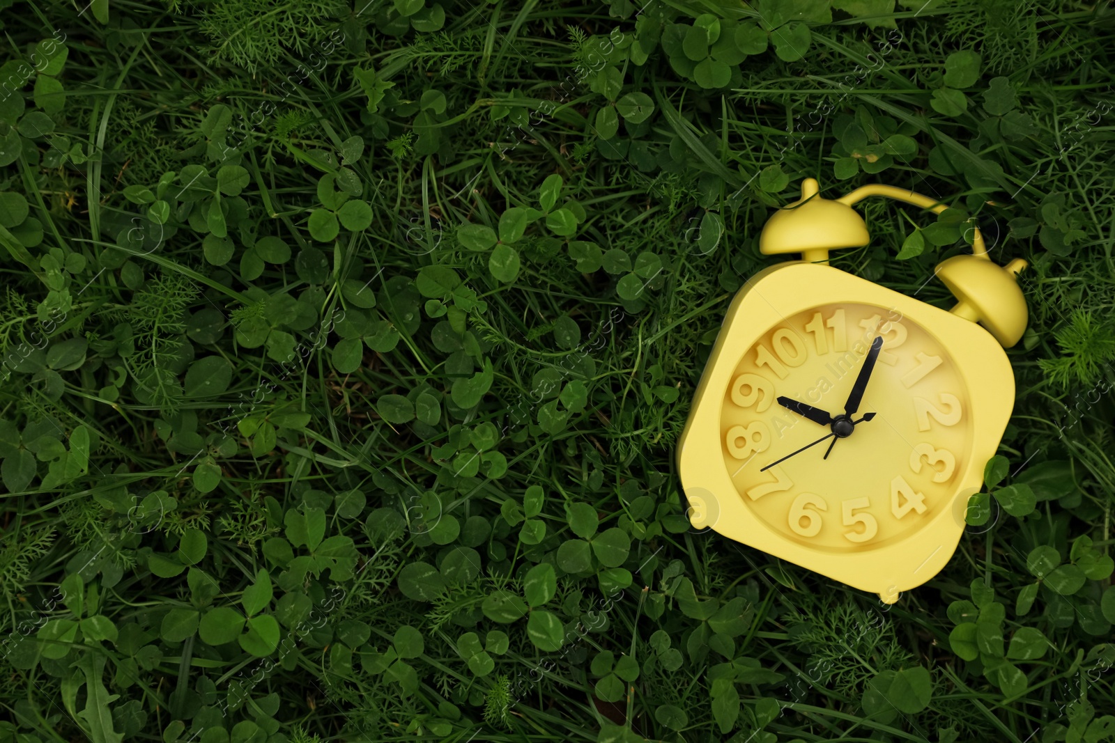 Photo of Yellow alarm clock on green grass outdoors, top view. Space for text