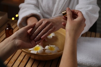 Photo of Woman receiving hand treatment at wooden table in spa, closeup
