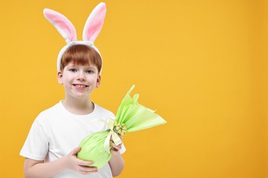 Easter celebration. Cute little boy with bunny ears and wrapped egg on orange background. Space for text