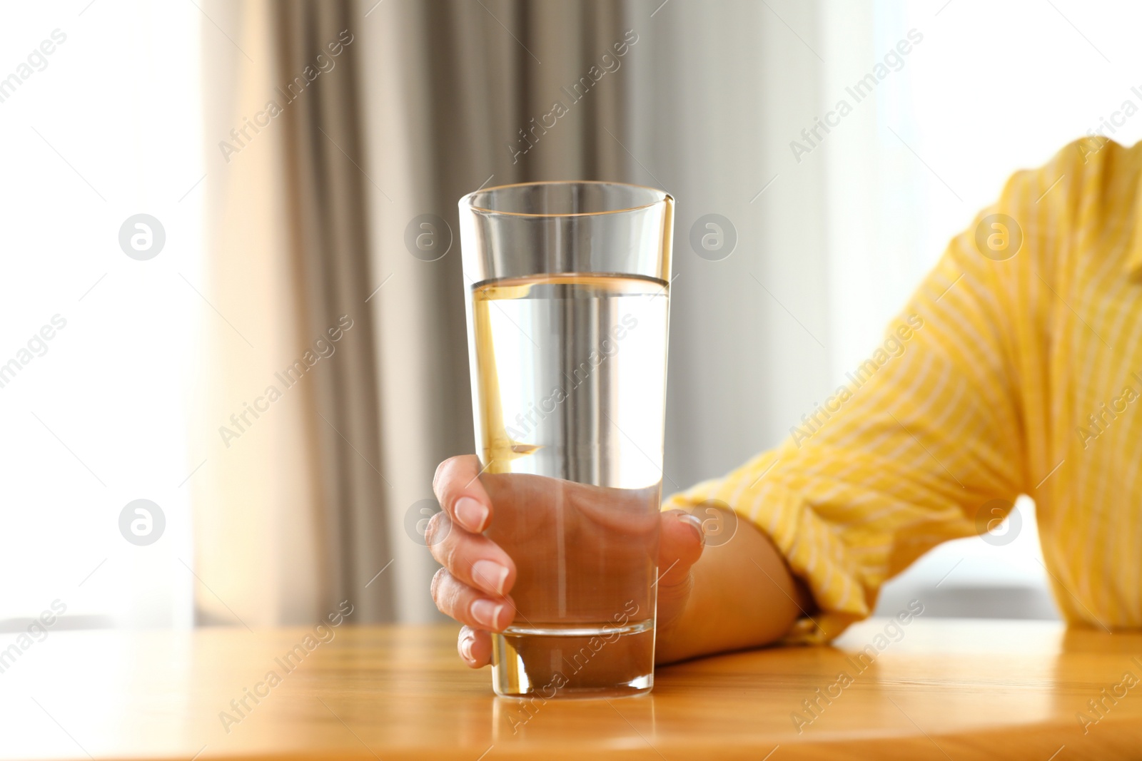 Photo of Woman holding glass of water at wooden table, closeup. Refreshing drink