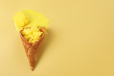 Photo of Melted ice cream in wafer cone on pale yellow background, top view. Space for text