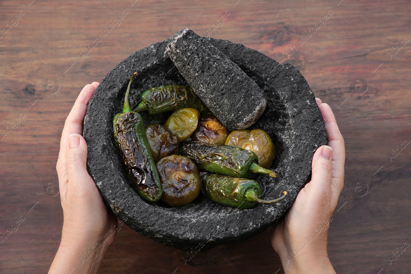 Photo of Woman holding mortar with ingredients for salsa sauce at wooden table, above view