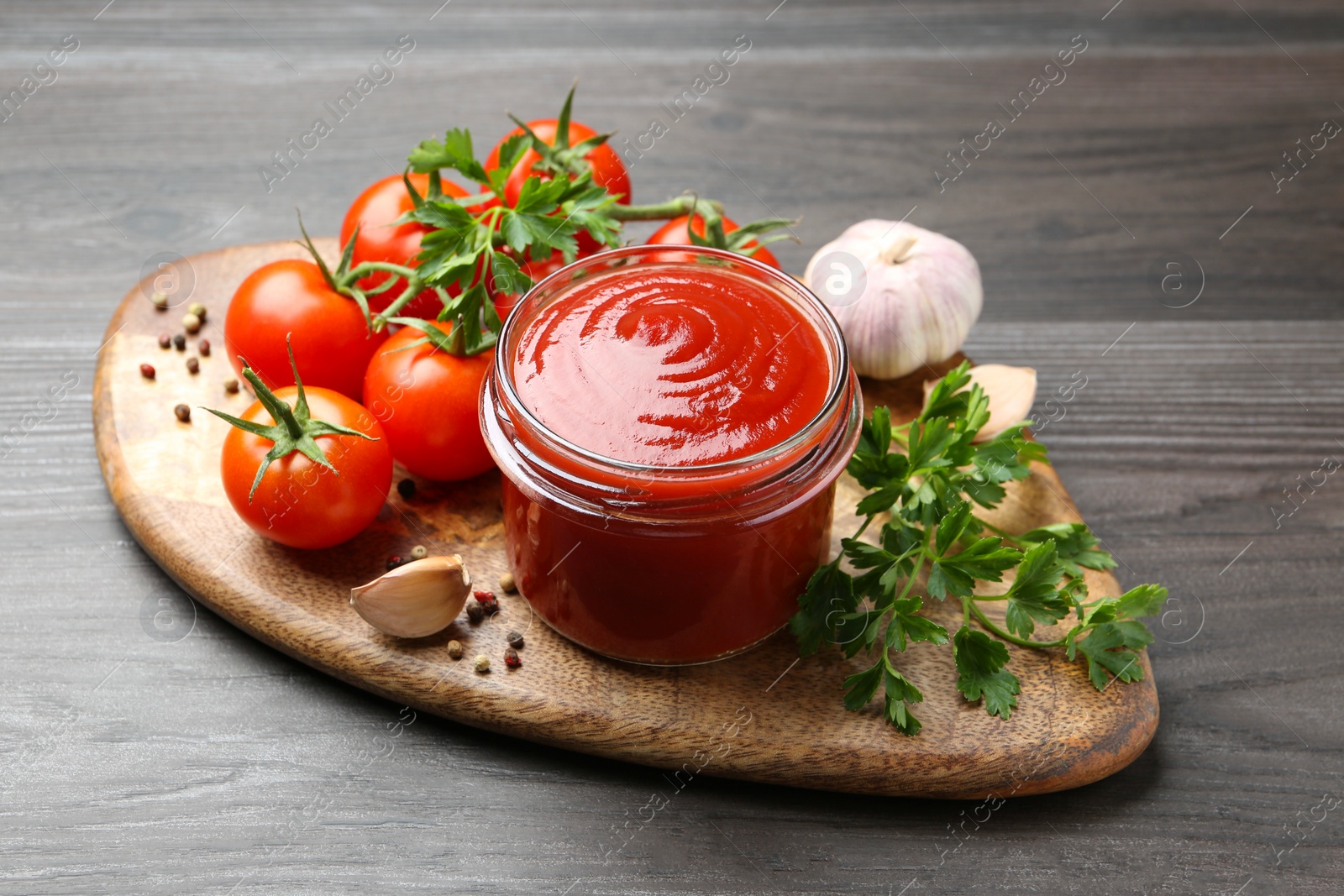 Tasty ketchup, fresh tomatoes, parsley and spices on grey wooden table Photo of Tasty ketchup, fresh tomatoes, parsley and spices on grey wooden table
