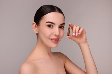 Beautiful young woman holding skincare ampoule on grey background