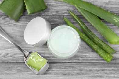 Photo of Jar with natural gel, spoon of peeled aloe vera and green leaves on light grey wooden table, flat lay
