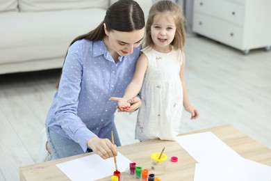 Photo of Mother and her little daughter painting with palms at home