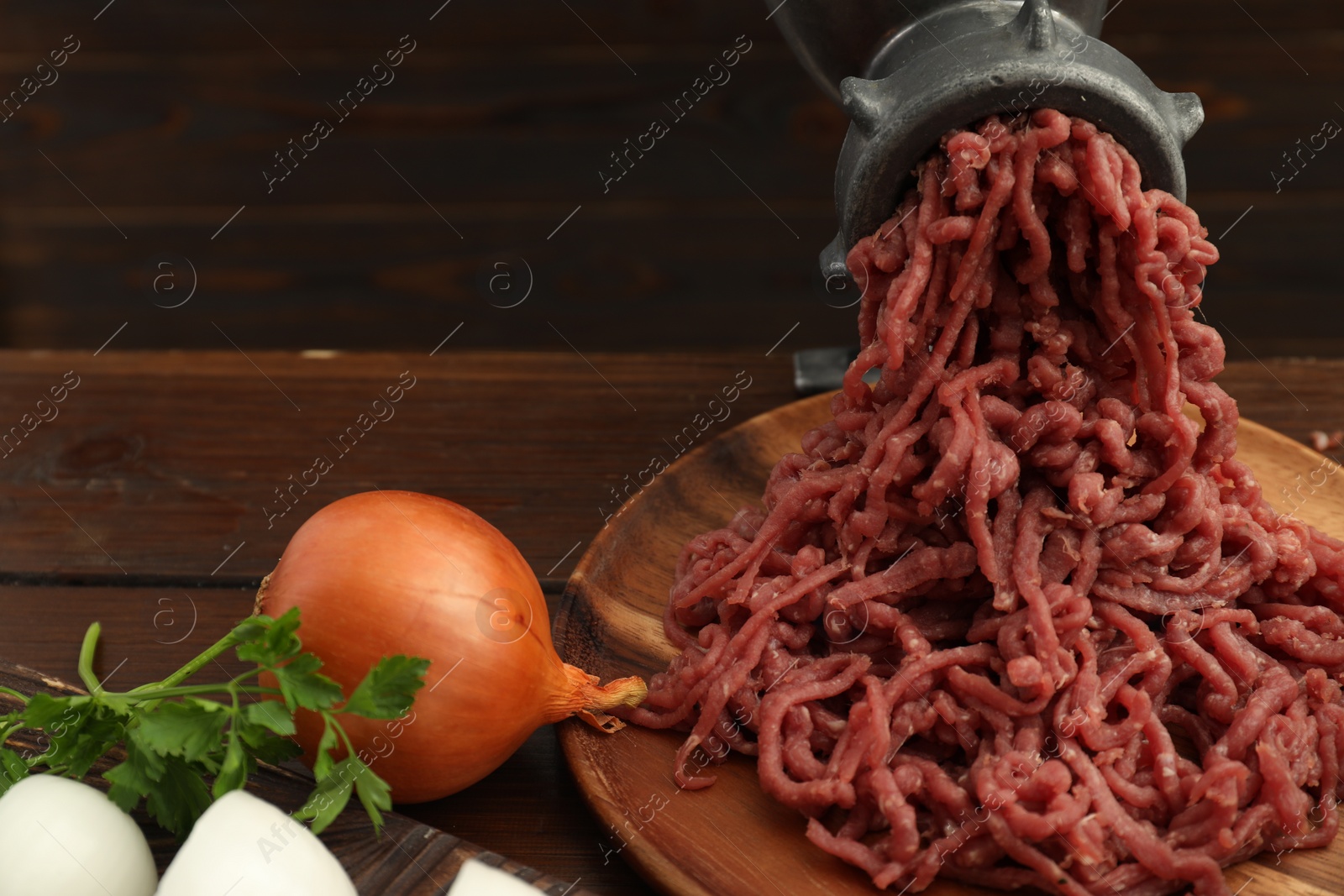 Photo of Meat grinder with beef mince, onion and parsley on wooden table, closeup