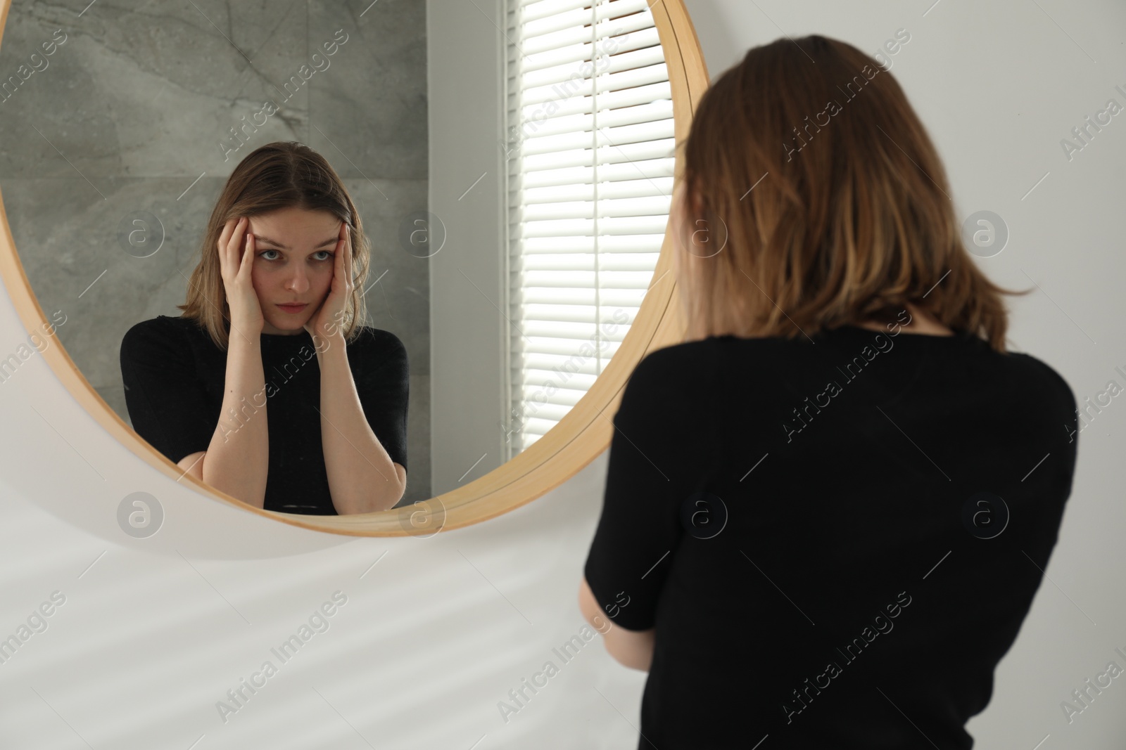 Photo of Sad young woman near mirror in room