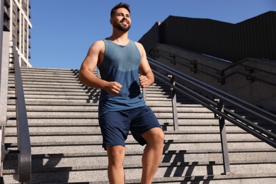 Happy man running down stairs outdoors on sunny day. Space for text