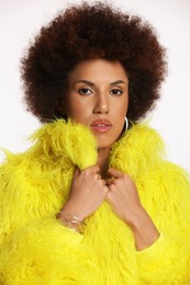 Portrait of beautiful young woman in stylish yellow fur coat on white background