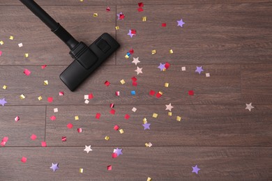 Photo of Vacuuming confetti from wooden floor, top view. Space for text