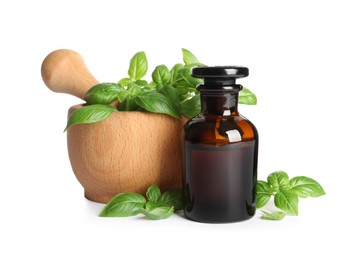 Photo of Bottle of basil essential oil near wooden mortar with leaves and pestle on white background